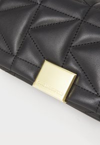 Clutch in pelle trapuntata nera con hardware dorato, dotato di una chiusura quadrata impressa con "KARL LAGERFELD". Superficie testurizzata con cuciture distinte.