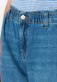 Denim teksased on lõdva lõikega, elastsete vöökohtadega, nööbikinnitusega ja klassikalise sinise värviga, millel on peened õmblusdetailid.