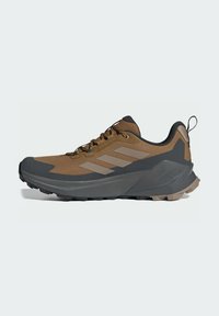 Brown hiking shoe with a textured fabric upper, black rubber outsole, and gray accents. Features sturdy laces and a pull tab at the heel.