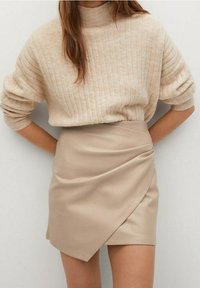 Beige geribbelde trui met een hoge halslijn, gedragen met een aansluitende beige nep leren rok met een voorste omslagontwerp en subtiele textuur details.