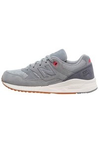 Grijze suède sneakers met gaasaccenten, voorzien van een witte tussenzool en een gumrubberen buitenzool. Contrasterende rode oogjes en merktekens.