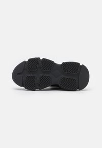 Semelle de chaussure de sport noire en caoutchouc texturé avec un motif en zigzag pour l'adhérence, orteil courbé et section de talon renforcée.
