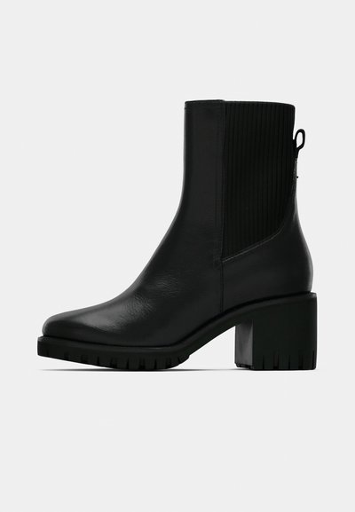 Bottine en cuir noir avec panneau latéral élastique côtelé, talon bloc et semelle texturée pour une meilleure adhérence. Finition lisse avec une garniture minimale.