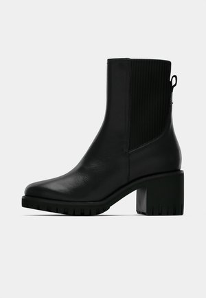 Bottine en cuir noir avec panneau latéral élastique côtelé, talon bloc et semelle texturée pour une meilleure adhérence. Finition lisse avec une garniture minimale.