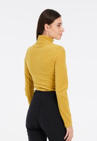 Maglione giallo a maniche lunghe e collo alto realizzato in tessuto morbido, con un design aderente e una texture liscia, abbinato a pantaloni neri a vita alta.