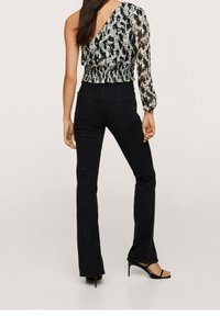 One-shoulder top in black and white abstract pattern, gathered waist, paired with black flared jeans and black heeled sandals.
