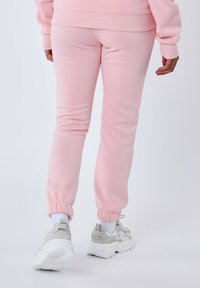 Pantalones de chándal rosa hechos de una tela suave, con puños y cinturilla elásticos. Combinados con zapatillas grises gruesas y calcetines blancos.