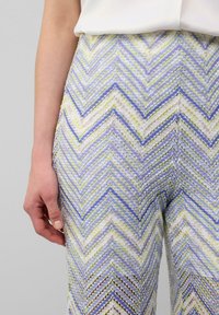 Pantalons élastiques tissés avec un motif chevron en lavande, vert et blanc. Le tissu présente une finition texturée et une coupe ajustée.