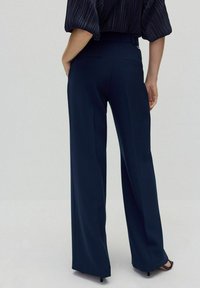 Marineblå vidde bukser lavet af glat stof, med en skræddersyet talje og to baglommer, stylet med en bluse med sorte striber.