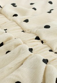 Tissu crème à pois noirs, présentant un motif texturé, froncé et plissé.