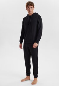 Czarny zestaw z bluzą i spodniami dresowymi wykonany z miękkiego, textured materiału. Bluza ma sznurek do regulacji, ściągacze przy mankietach oraz dopasowaną talię.