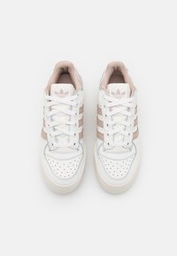 White athletic sneakers made of leather and synthetic materials, featuring three pink stripes, round toe, and perforated detailing on the toe box.