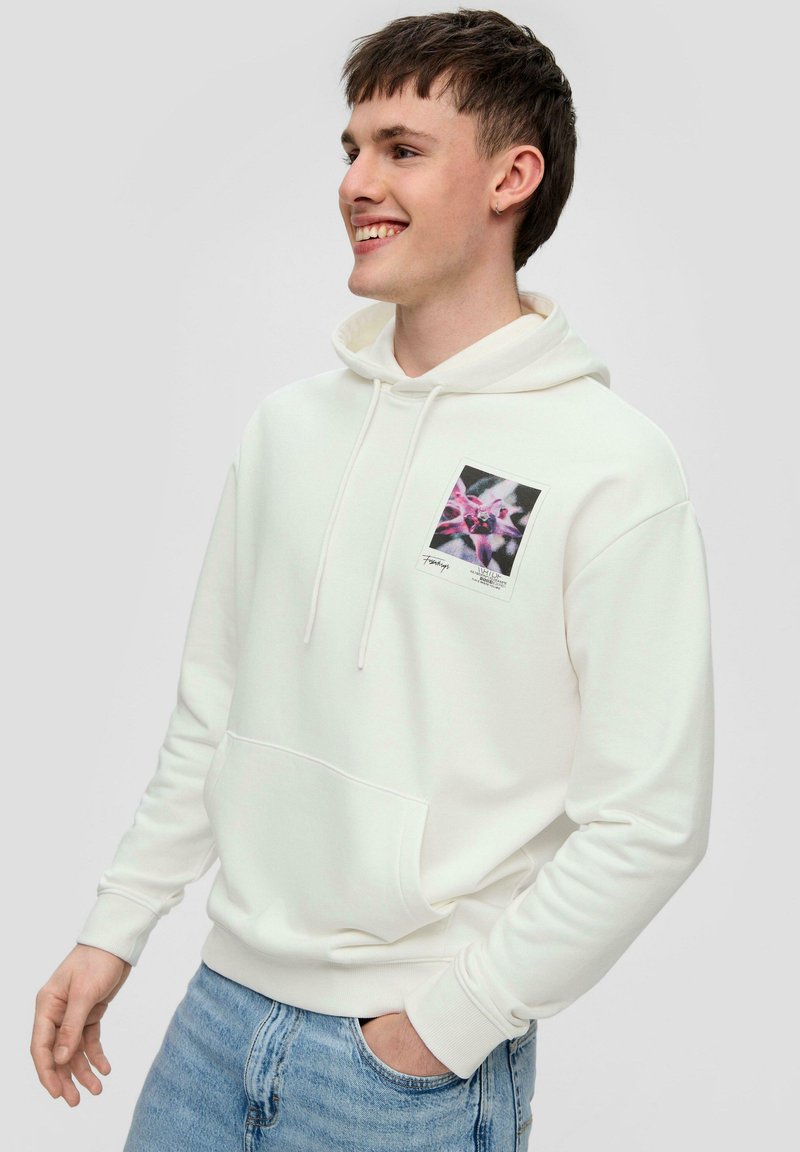 Sudadera blanca con capucha, con un bolsillo delantero y una impresión gráfica colorida en el pecho izquierdo. La tela parece suave y casual.