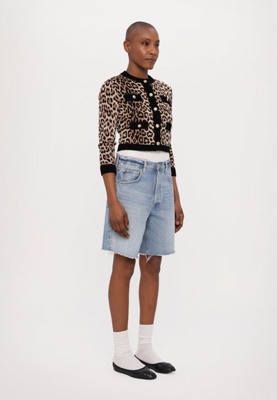 Cardigan cu imprimeu leopard, cu accente negre și nasturi aurii, asortat cu șorturi din denim de culoare albastră deschis, cu margini destrămate. Pantofi plată negri și sosete gri.