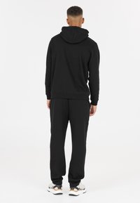 Completo con felpa nera e pantaloni tuta in tessuto morbido. Presenta una tasca a marsupio e polsini a coste. Accentuato da sneakers chiare.