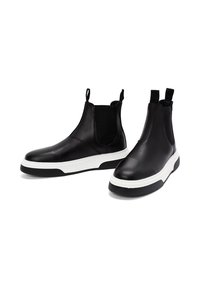 Botas Chelsea de piel negra con suelas de goma gruesas en blanco y negro, paneles laterales elásticos y lengüetas en la parte superior.