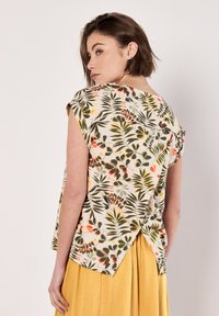 Blusa de manga corta con estampado floral que presenta un fondo beige con patrones de hojas en verde, naranja y rojo, y un diseño de apertura única en la parte trasera.