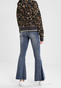 Sweatshirt à capuche en imprimé camouflage avec un design court et un ourlet côtelé, associé à un jean évasé avec des chevilles fendues et une texture bleu délavé.