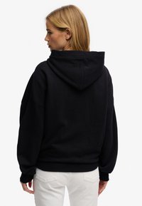 Czarna bluza z kapturem o luźnym kroju, z prążkowanymi mankietami i fakturowaną tkaniną. Posiada kieszeń i subtelne detale przeszyć.