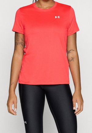 Persoon die een felrode sportshirt met korte mouwen en zwarte legging draagt met zichtbare Under Armour-logo's op shirt en broek.