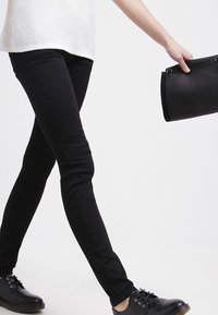 Jeans negros ajustados con una textura suave y una cintura de altura media, combinados con zapatos negros de cordones y un bolso negro estructurado.