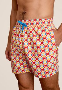 Rode zwembroek met een geometrisch patroon van gele en blauwe driehoeken. Voorzien van een elastische tailleband met een blauwe trekkoord en zijzakken.