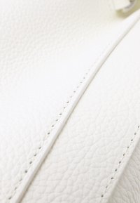 Textura de cuero blanco con un sutil patrón de guijarros, con costuras limpias y un acabado suave, que muestra la calidad del material.