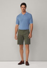 Blå strikket polo med korte ærmer og krave, parret med grønne shorts og afsluttet med brune loafers. Simpelt og moderne design.