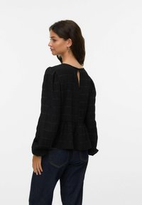 Zwarte blouse met textuurstrepen, peplum taille en keyhole rugdetail. Lange mouwen met een lichte puff, gedragen met donkerblauwe jeans.