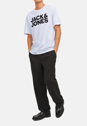 Weißes Kurzarm-T-Shirt mit auffälligem schwarzen "JACK & JONES"-Text, kombiniert mit lockeren schwarzen Hosen und schwarzen Schuhen, die einen lässigen Schnitt zeigen.
