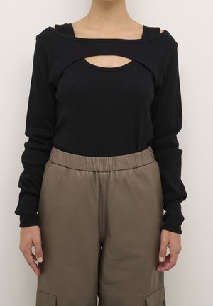 Haut noir à manches longues avec une découpe au niveau de la poitrine, associé à un pantalon en cuir taupe taille haute avec une ceinture élastique.
