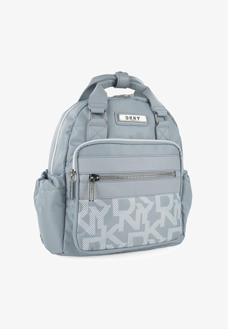 Mochila azul clara con un acabado texturizado, que cuenta con un bolsillo frontal con cremallera y un patrón de logotipos repetido. Incluye correas ajustables.
