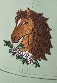 Grüne Kappe mit einem braunen gestickten Pferdekopf und floralem Akzent aus pinken Blumen und grünen Blättern am Boden.