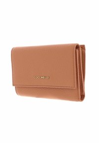 Portefeuille en cuir texturé beige avec un design pliable et un logo doré "COCCINELLE" sur le rabat avant.