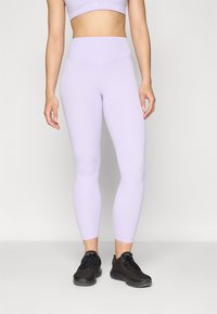 Leggings attivi color lilla con vita alta, texture liscia e design aderente. Abbinati a scarpe da ginnastica nere.
