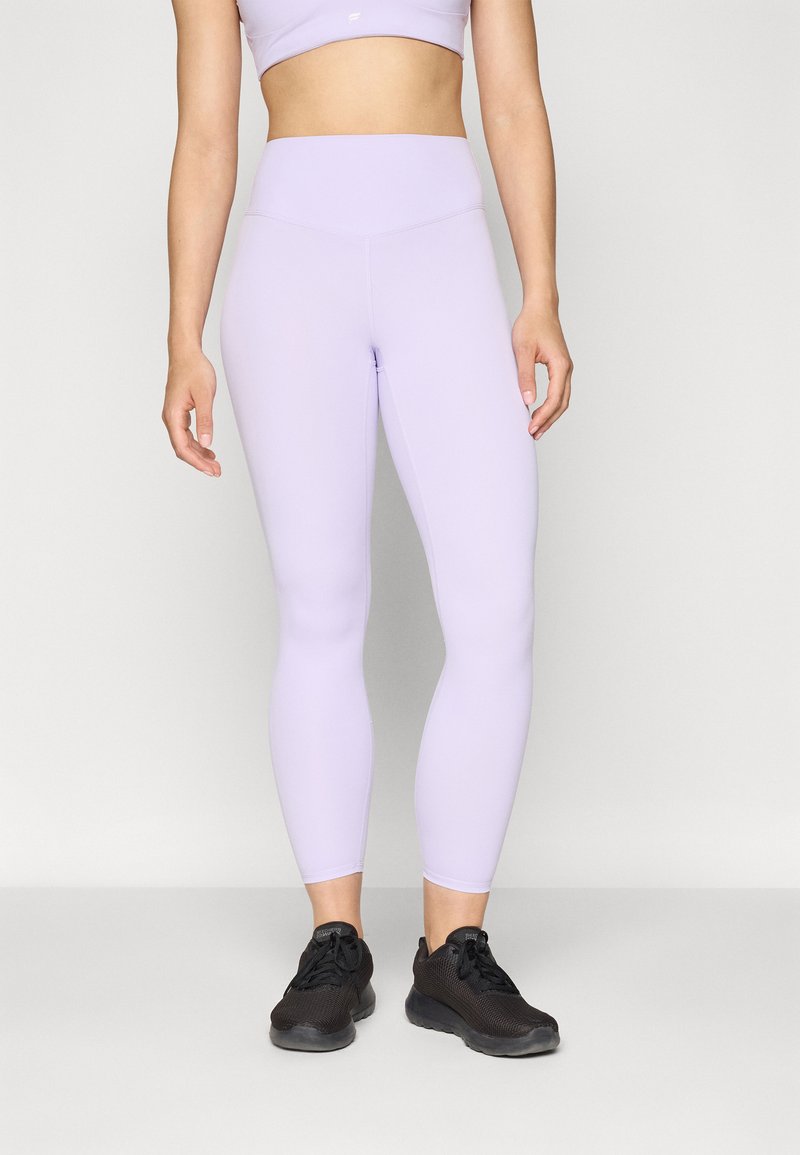 Leggings attivi color lilla con vita alta, texture liscia e design aderente. Abbinati a scarpe da ginnastica nere.