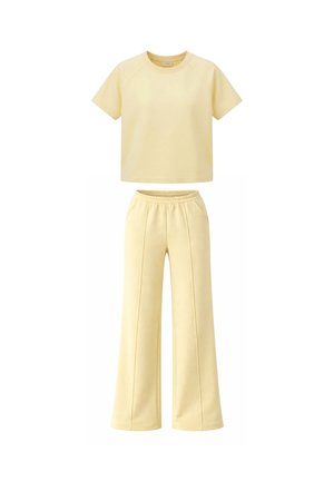 Sárga rövid ujjú, kerek nyakú felső, magasderekú, széles szárú nadrággal, rugalmas derékrésszel és az elülső varrás részleteivel párosítva.