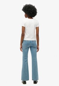 Camiseta blanca de manga corta combinada con unos jeans acampanados de color azul claro. El conjunto presenta una silueta ajustada y denim con una textura sutil.