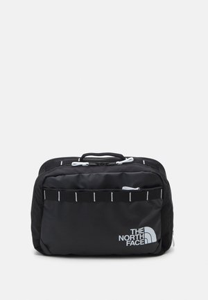Schwarze rechteckige Reisetasche mit Griff, vorne Reißverschlusstasche, weißen Reißverschlussziehern und "The North Face" Logo auf der Vorderseite unten rechts.