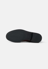 Semelle en caoutchouc noir avec des motifs de grip texturés, présentant une section de talon légèrement surélevée et un bord propre et lisse.