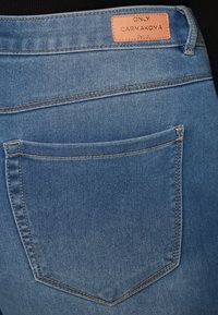 Μπλε τζιν παντελόνι με πίσω τσέπη, διακοσμημένο με πορτοκαλί ραφές και ετικέτα από δέρμα που αναγράφει "ONLY CARMAKOMA." Κλασικό στυλ με πέντε τσέπες.