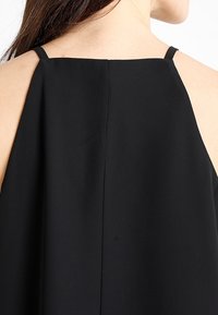 Indumento nero senza maniche con spalline sottili, caratterizzato da una trama liscia e un design con apertura a chiave sulla schiena. Stile semplice e minimalista.