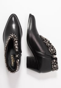 Botas de cuero negro hasta el tobillo con punta afilada, adornadas con strass a lo largo de los lados, cierre de cremallera y tacón cuadrado.