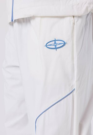 Witte broek met een blauw en wit PXP-logo patch en blauwe pipings aan de zijnaad.