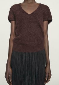 Maglione corto bordeaux a maniche corte in morbido e peloso tessuto con scollatura a V e orlo a coste, abbinato a una gonna plissettata nera.