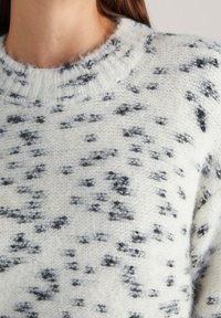 Maglione lavorato a maglia in crema con motivo a macchie nere. Collo rotondo, texture morbida e finitura leggermente pelosa. Design casual, maniche lunghe.