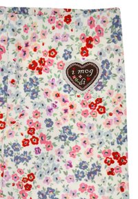 Stoff mit Blumenmuster, der kleine rote, pinke und blaue Blumen auf weißem Hintergrund zeigt. Enthält ein braunes herzförmiges Patch mit Text.