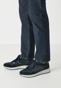 Dunkelblaue Sneakers aus einer Materialkombination von Wildleder und Mesh, mit schwarzen Akzenten und einer weißen Sohle, getragen mit dunklen Jeans.