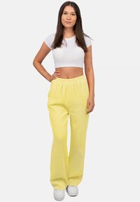 Gelbe, strukturierte, weit geschnittene Hose mit elastischem Bund, kombiniert mit einem enganliegenden weißen Crop-Top und weißen Sneakers.