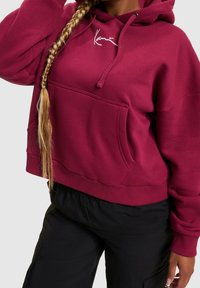 Bordeauxroter Hoodie aus weicher Baumwolle mit einer Fronttasche, Kapuze mit Kordelzug und weißem Logoaufdruck auf der Brust. Mit gerippten Bündchen und Saum.